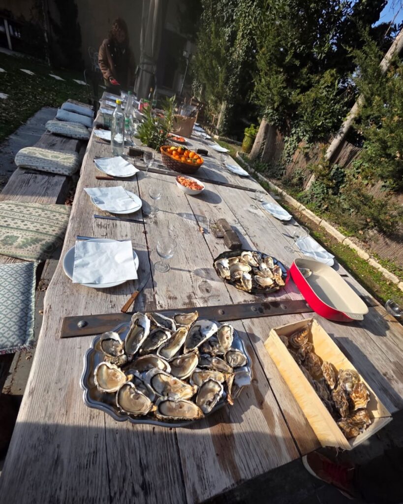 Longue table en bois dressée en extérieur avec des plateaux d'huîtres fraîches, des verres, des assiettes et un panier de kumquats sous le soleil d'hiver en Provence, au Mas de la Sacristière.